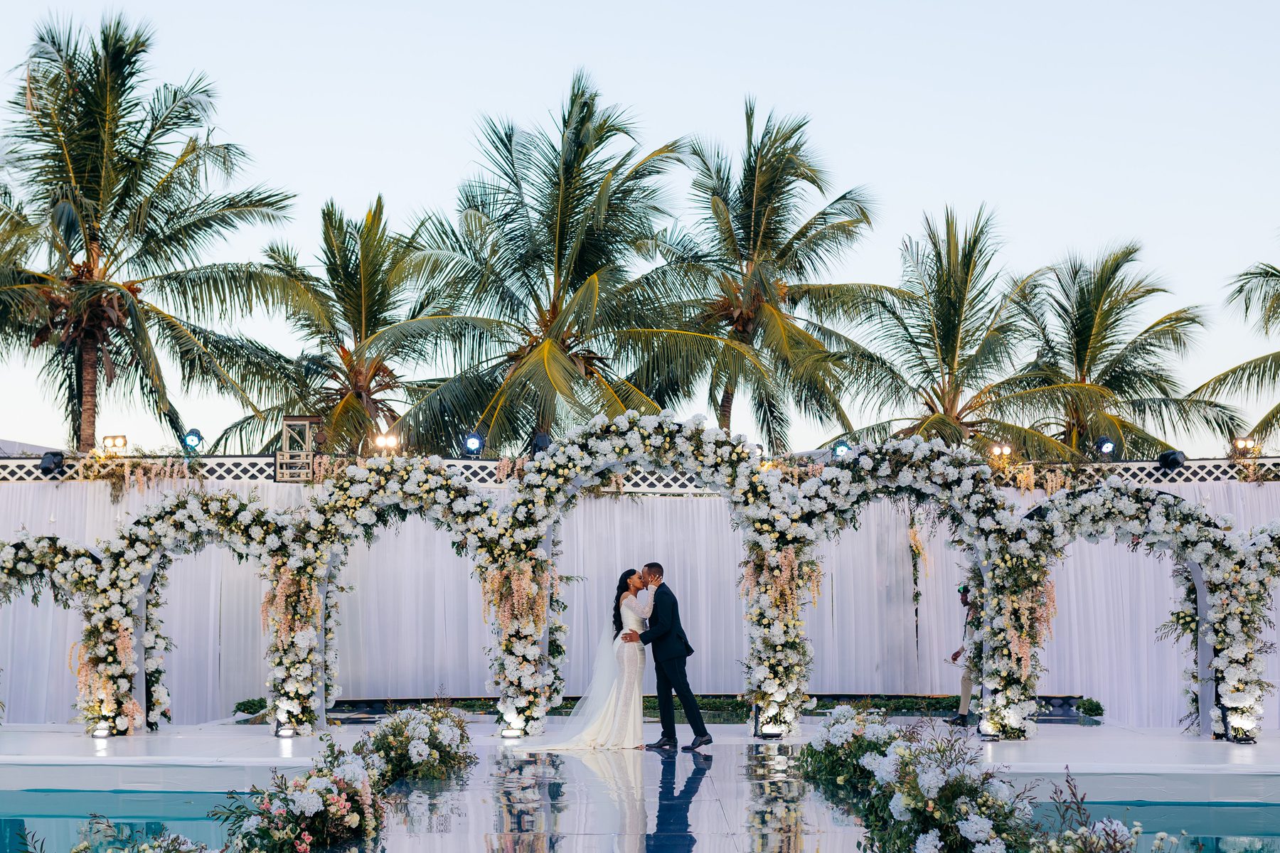 Ali & Dr. Lucy — the couple beneath the floral archway on the Tanga coastline, by Kevins Events